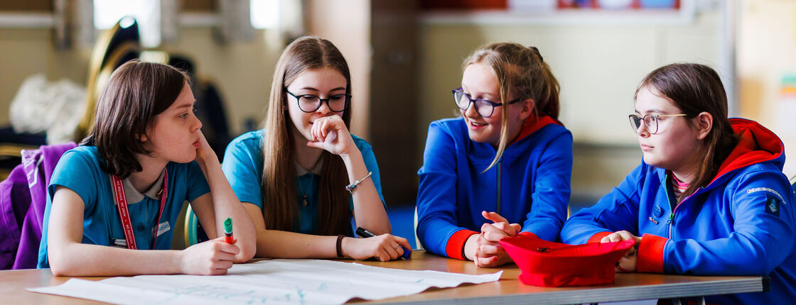 4 young leaders are sat aorund a table with a map in front of them, laughing and having a conversations.